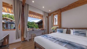 A bedroom with a large bed, wooden beams, a window with a view of a house, and a small table with a vase.