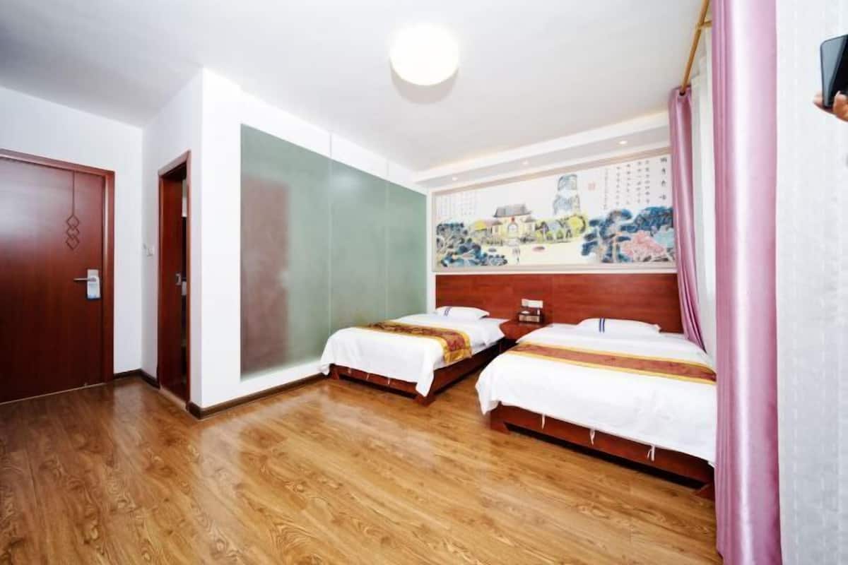 Habitación de hotel con dos camas, suelo de madera, un ventanal grande y un cuadro en la pared.