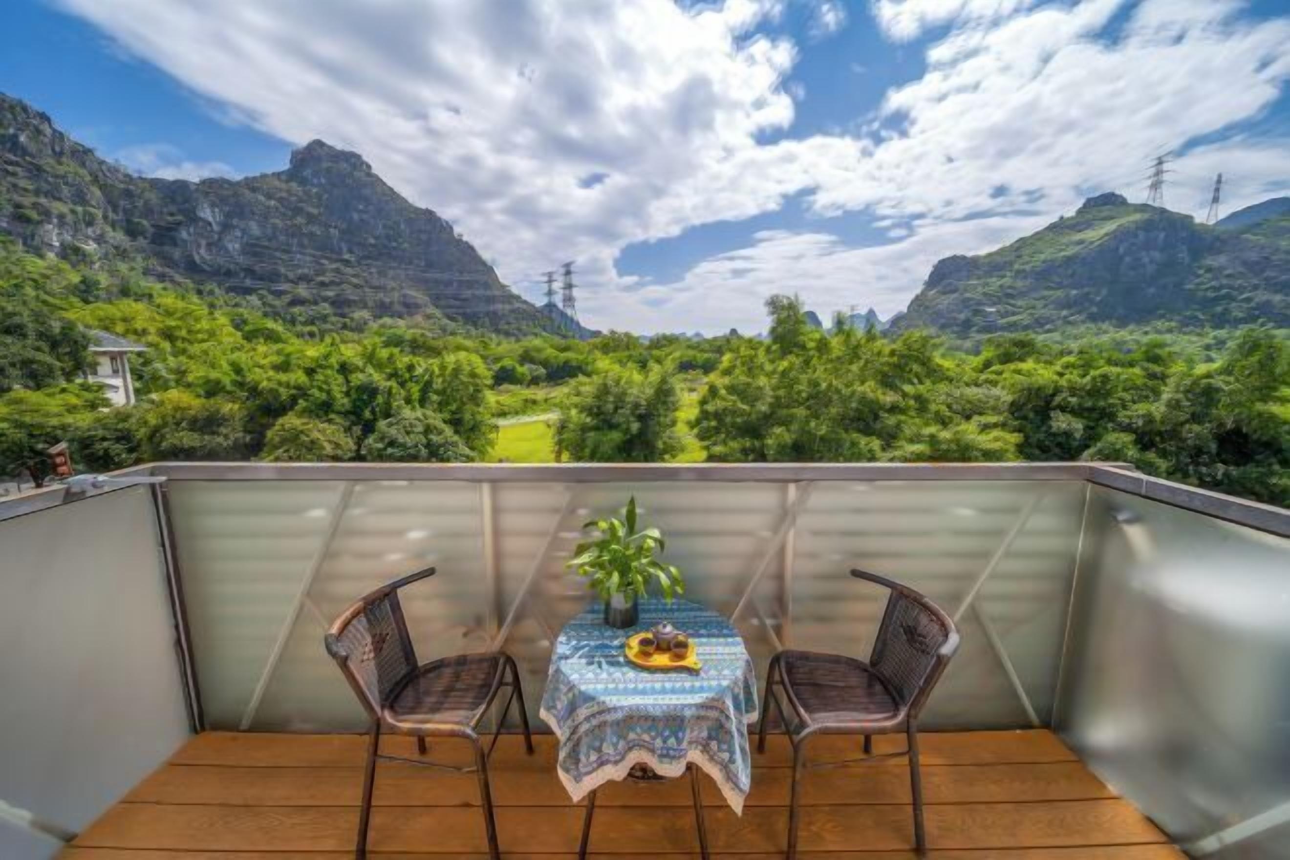A balcony with a table and chairs, overlooking a mountainous landscape with greenery and power lines.