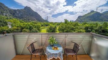 A balcony with a table and chairs, overlooking a mountainous landscape with greenery and power lines.