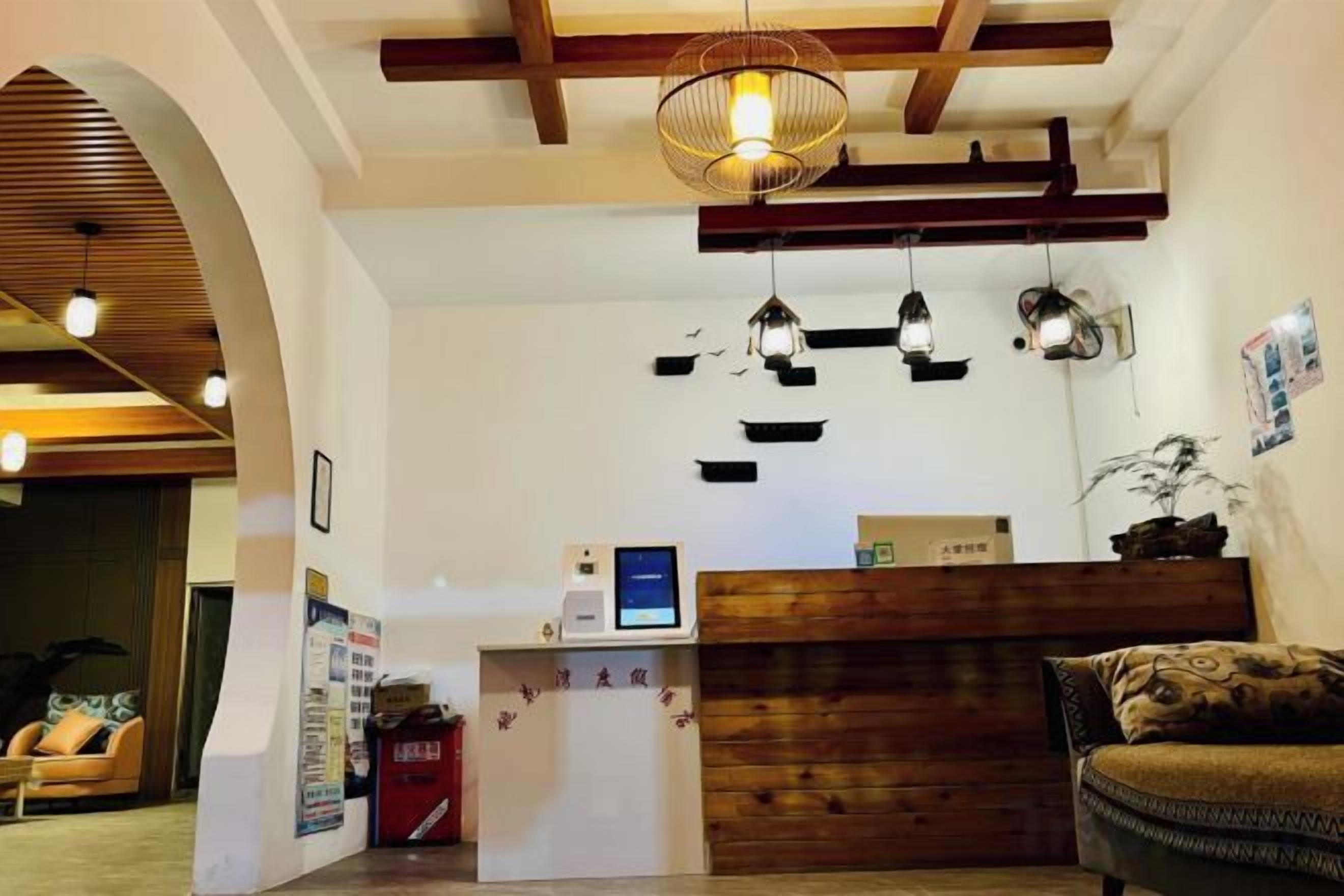 Zona de recepción con un mostrador de madera, una pantalla digital y una lámpara colgante.