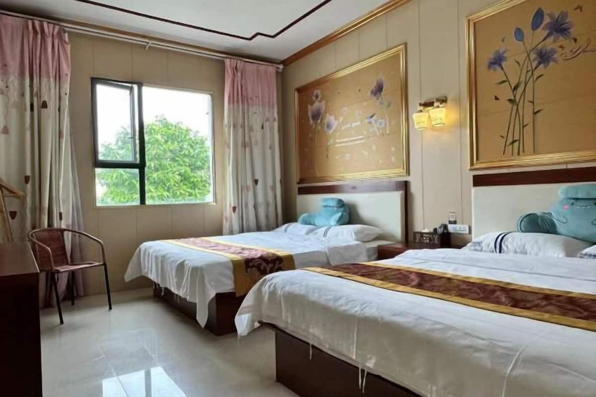 Habitación de hotel con dos camas, un escritorio y una silla. Hay cortinas, una ventana y decoración en la pared.
