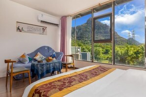 A hotel room with a bed, a sofa, a small table, and a view of mountains and greenery. - Peach Blossom Bay Resort (Guilin Ludiyan Scenic Area) (Guilin)