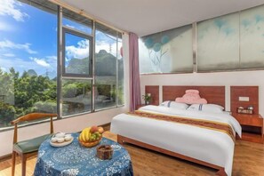 A bedroom with a large window, a bed with a pink pillow, a bedside table, and a table with fruit and a bowl. - Peach Blossom Bay Resort (Guilin Ludiyan Scenic Area) (Guilin)