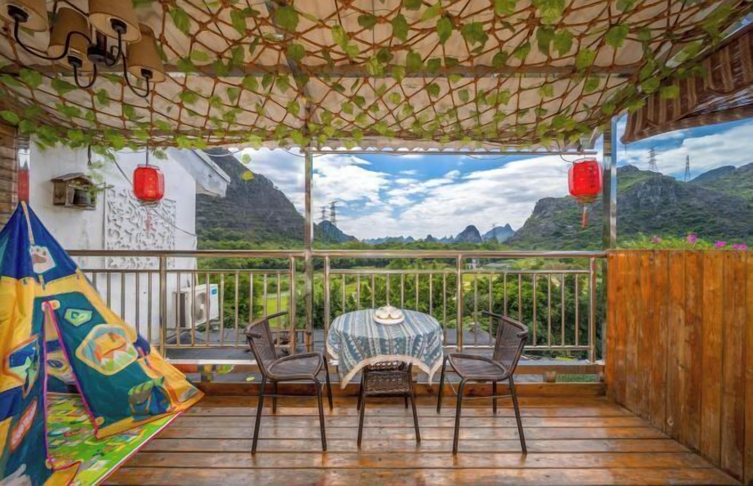 Een balkon met een tafel en stoelen, uitzicht op bergen en een rode lantaarn.