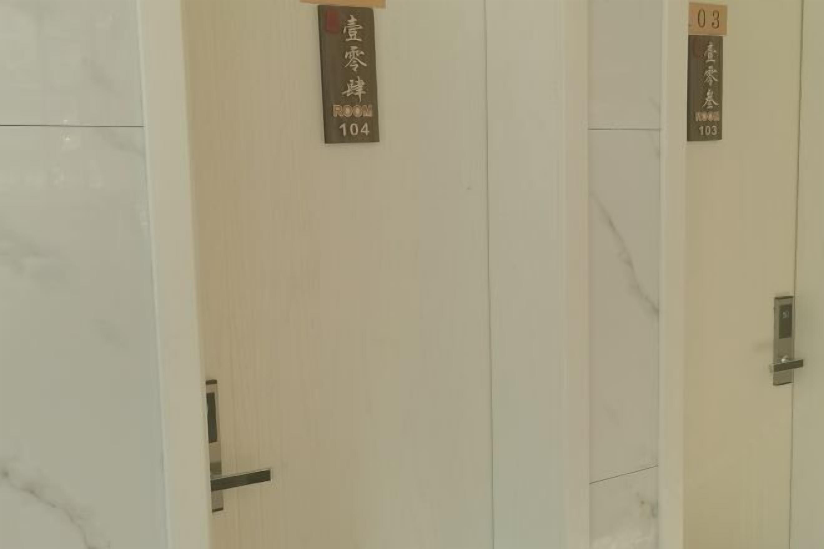 A hotel room with a marble wall and a door with a sign indicating room number 104.