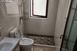 Et badeværelse med toilet, brusebad og et lille vindue.