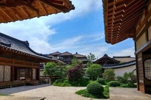 Um pátio japonês tradicional com edifícios de madeira, um caminho de cascalho e vegetação bem cuidada.