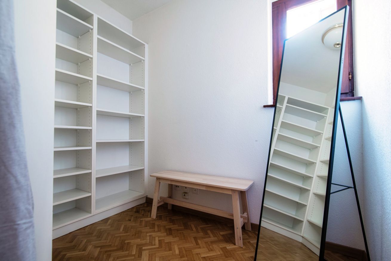 Une pièce avec un banc en bois, un miroir et des étagères blanches.