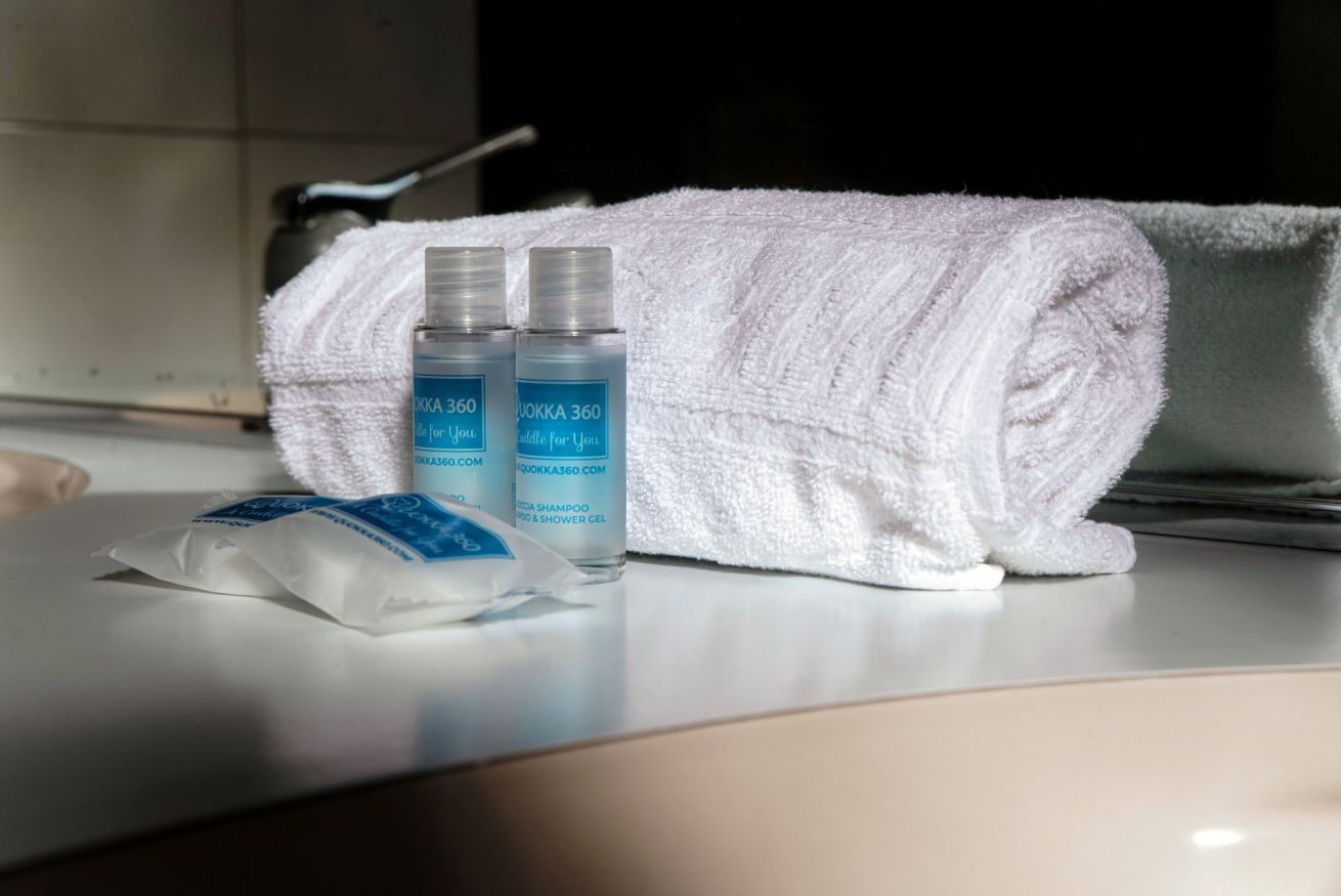 A bathroom with a white towel, two bottles of shampoo, and a packet of soap.
