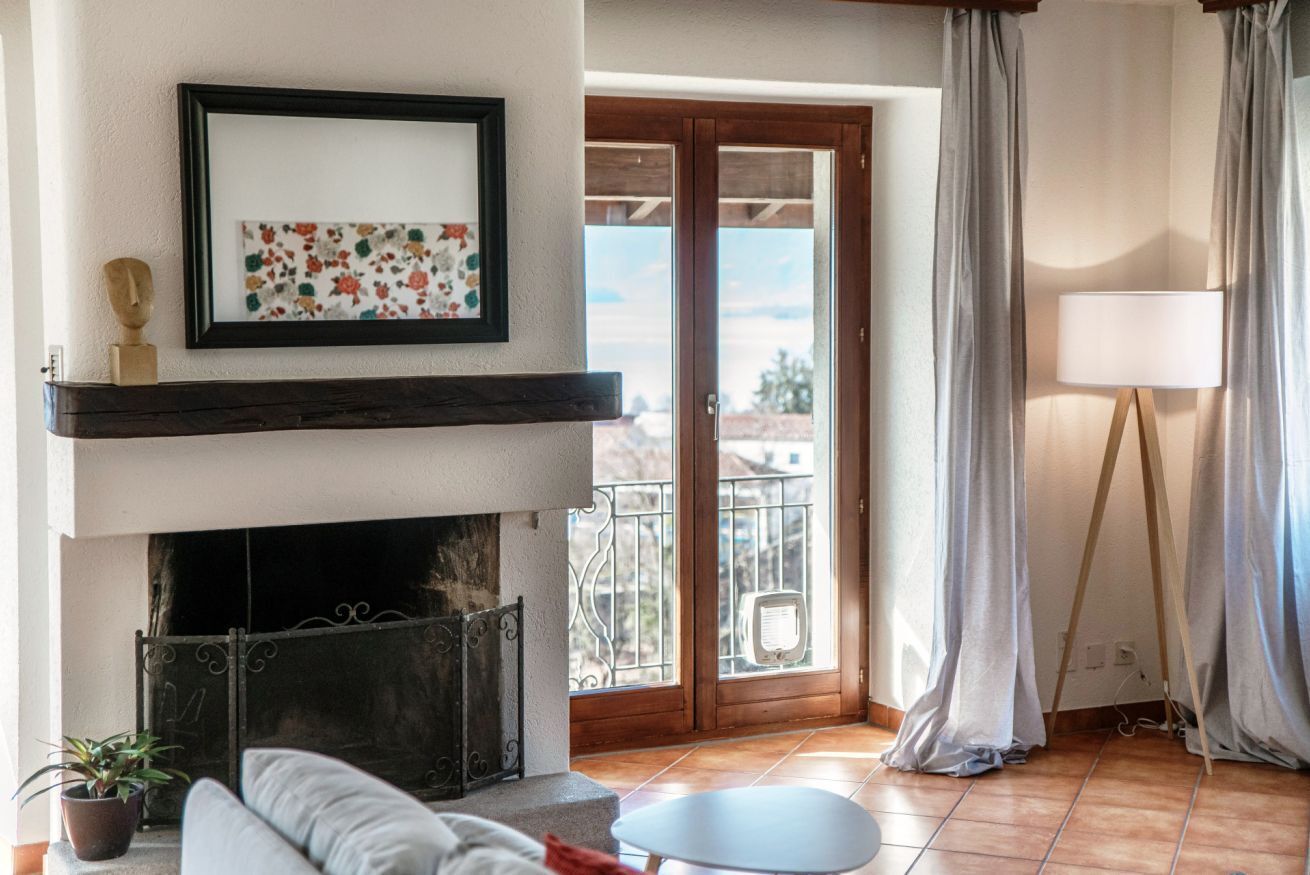 A living room with a fireplace, a sofa, a small table, and a balcony with curtains.