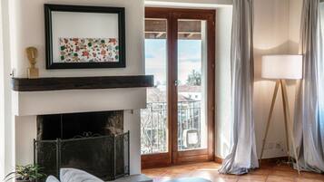 A living room with a fireplace, a sofa, a small table, and a balcony with curtains.