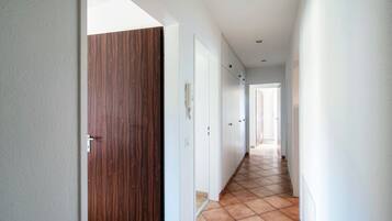 Un corridoio con una porta in legno, pareti bianche e pavimento piastrellato.