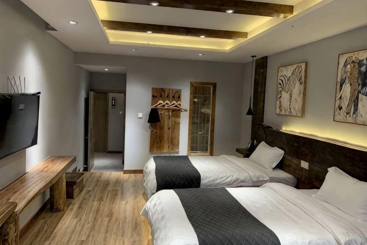 Ein modernes Hotelzimmer mit zwei Betten, einem Fernseher, Holzböden und Kunstwerken an den Wänden.