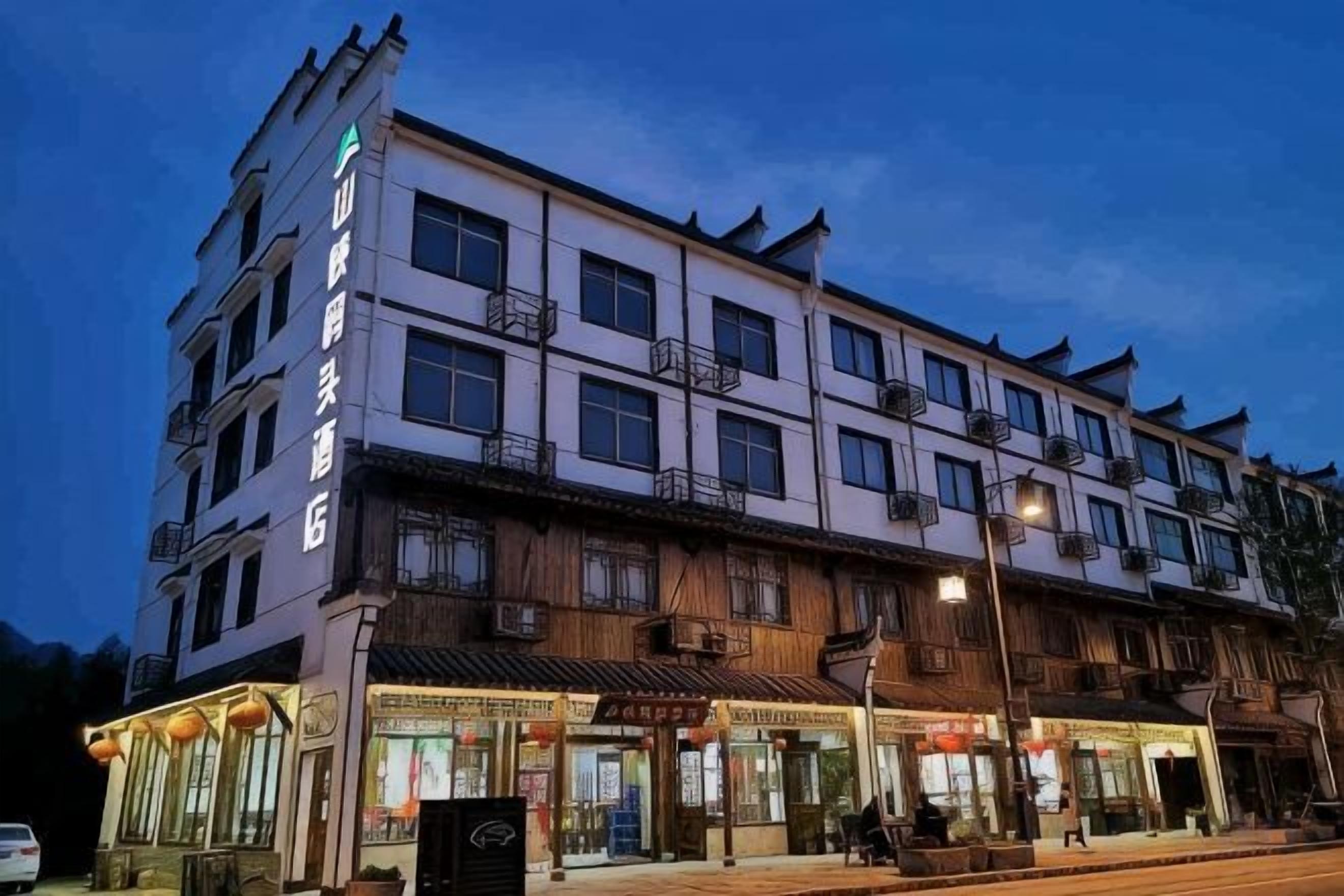 A multi-story hotel with a traditional architectural style, featuring balconies and a ground-level commercial area with shops.
