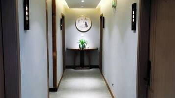 A narrow hallway with a clock on the wall, a small table with a plant, and a door at the end.