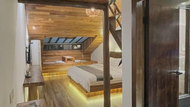 Une chambre confortable avec un plafond en pente, un plancher en bois, un lit, une petite table et un luminaire suspendu.