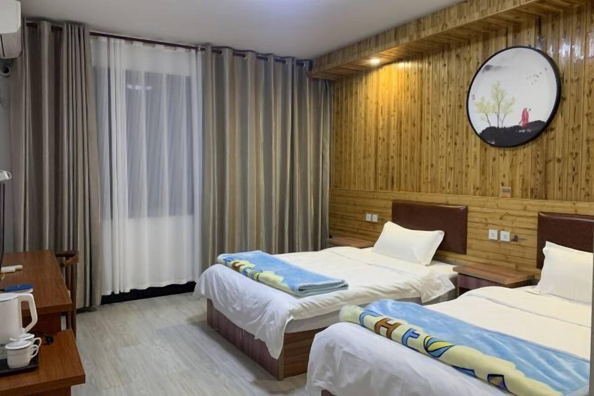 Ein Hotelzimmer mit zwei Betten, einem Holzkopfteil, einem runden Spiegel und einem Schreibtisch mit Kaffeemaschine.