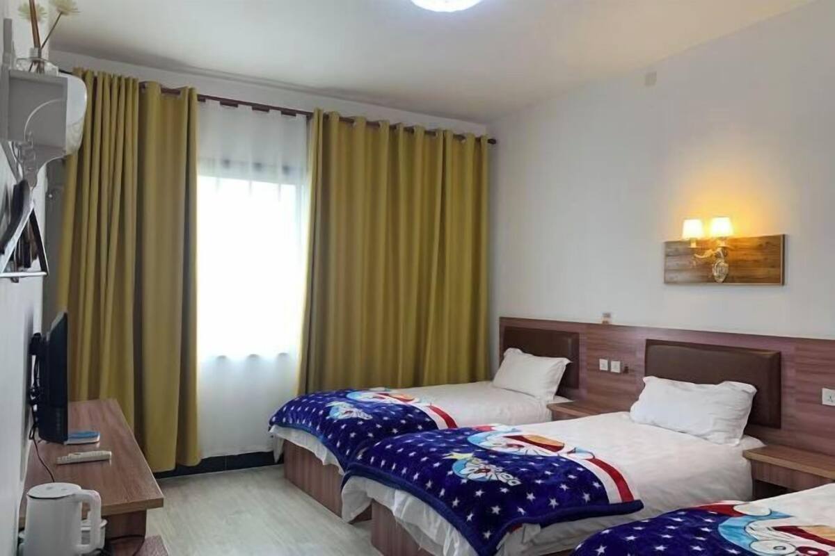 Ein Hotelzimmer mit zwei Betten, einem Schreibtisch mit Computer, einer Lampe und einem Vorhangfenster.