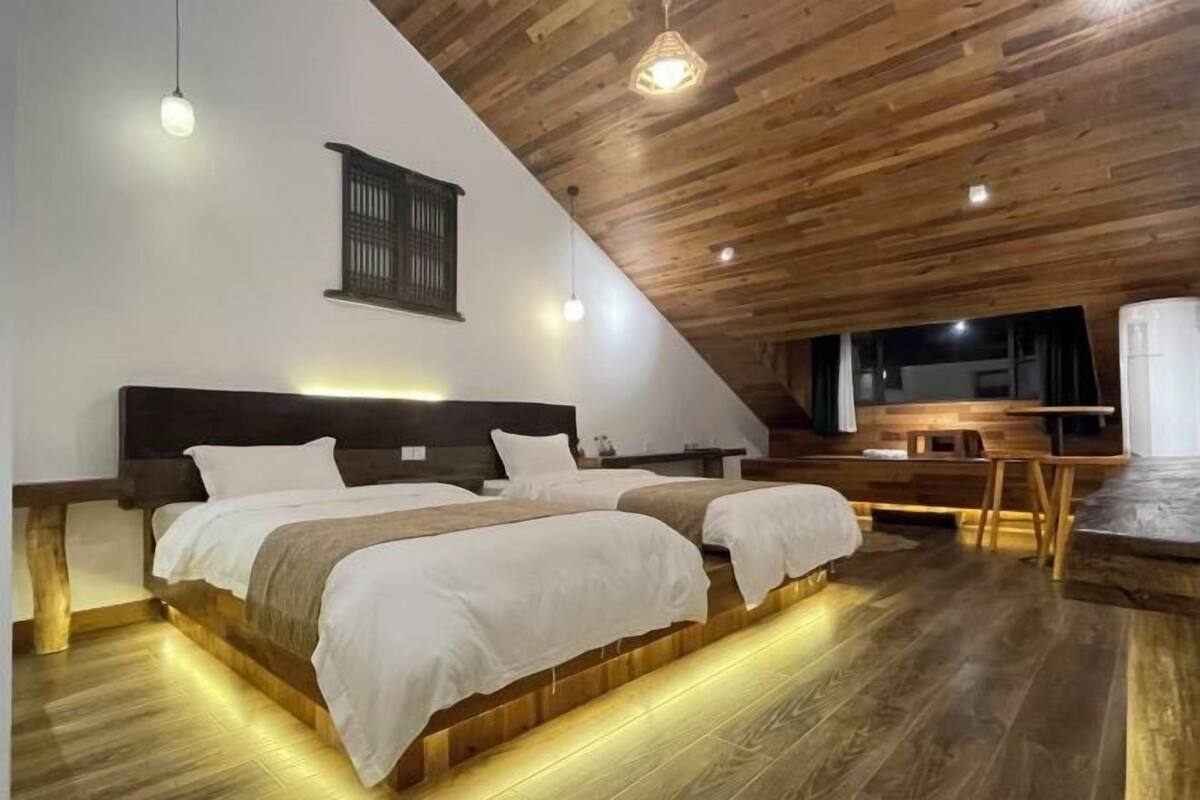 Ein Schlafzimmer mit zwei Betten, Holzboden, schrägem Dach und einem kleinen Tisch mit Stühlen.