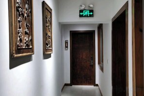 A hallway with a wooden door at the end, framed artwork on the walls, and a green exit sign above. - Shanxian Matou Inn (Hangzhou)