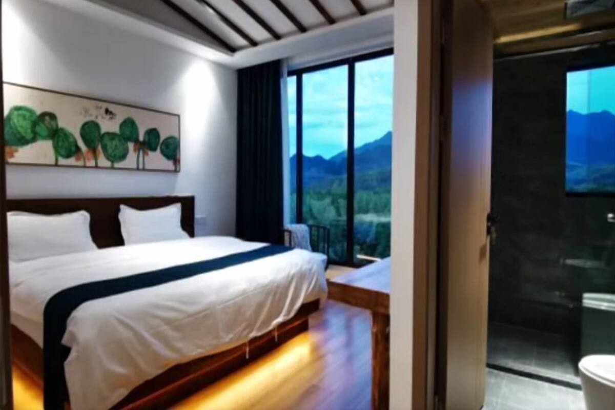 Ein Schlafzimmer mit einem großen Bett, Blick auf Berge durch ein Fenster und einem Bild an der Wand.