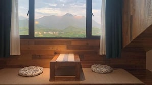 Une pièce avec un banc en bois, deux coussins à motifs et une vue sur les montagnes par une grande fenêtre.