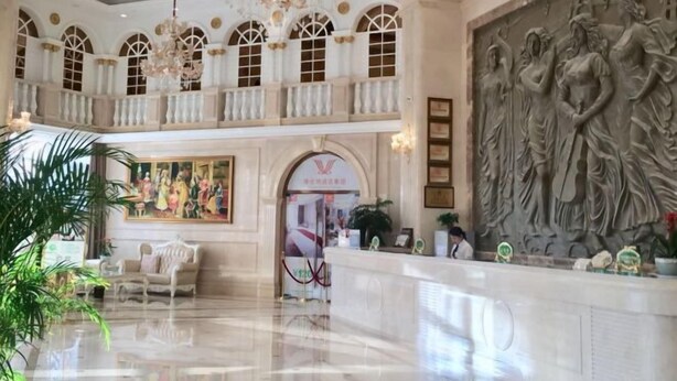 A spacious lobby with a high ceiling, chandeliers, a reception desk, and a large mural.