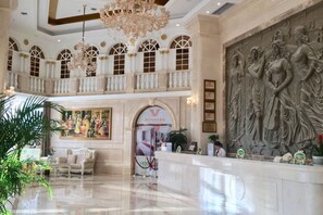 A spacious lobby with a high ceiling, chandeliers, a reception desk, and a large mural.
