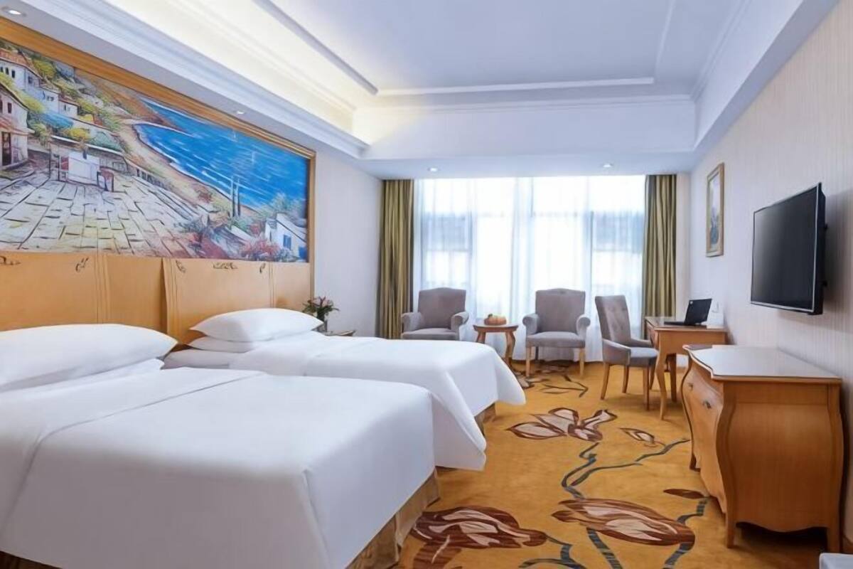 Habitación de hotel con dos camas, un escritorio, un televisor y un mural en la pared.