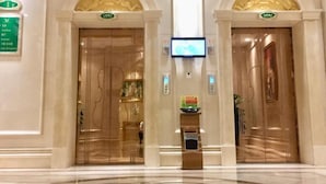 A hotel lobby with two elevators, a digital display, and a reception desk.