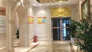 A hotel lobby with a grand chandelier, a glass elevator, and a decorative wall.