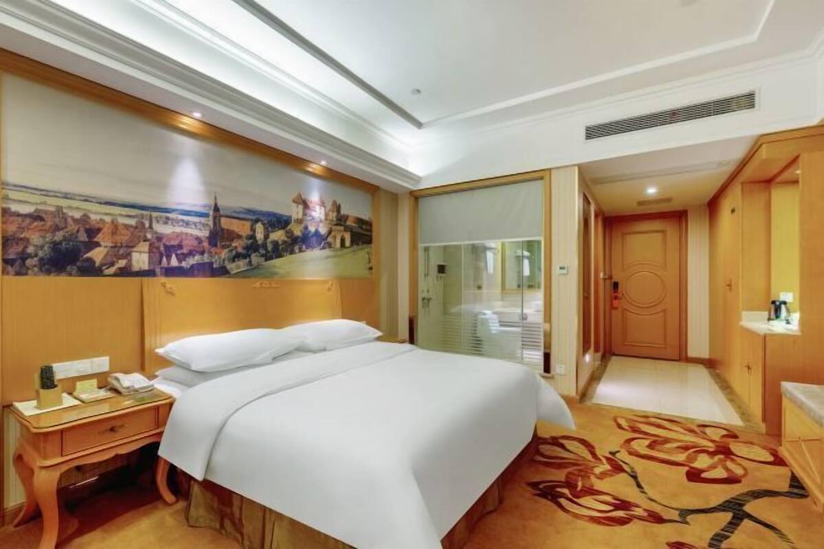 Habitación de hotel con una cama grande, una mesita de noche, un escritorio, un cuadro en la pared y una puerta que da a un baño.