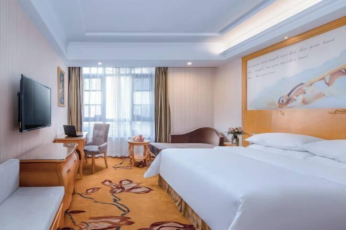Habitación de hotel con cama, escritorio, silla, televisión y ventana con cortinas.