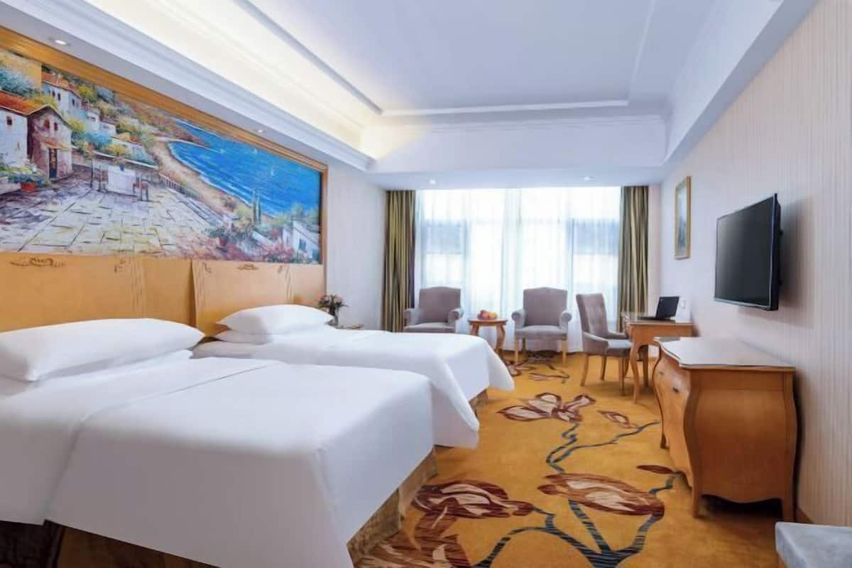 Una habitación de hotel con dos camas, un escritorio, un televisor y un cuadro en la pared.