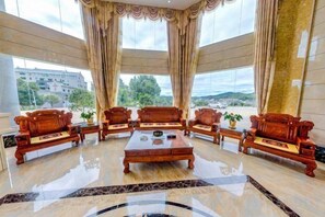 A spacious lobby with a central coffee table surrounded by wooden sofas, large windows with curtains, and a view of the outside. - Hongdou Mountain Villa (Pingyuan)