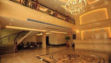 A grand lobby with a marble floor, a staircase, and a chandelier.