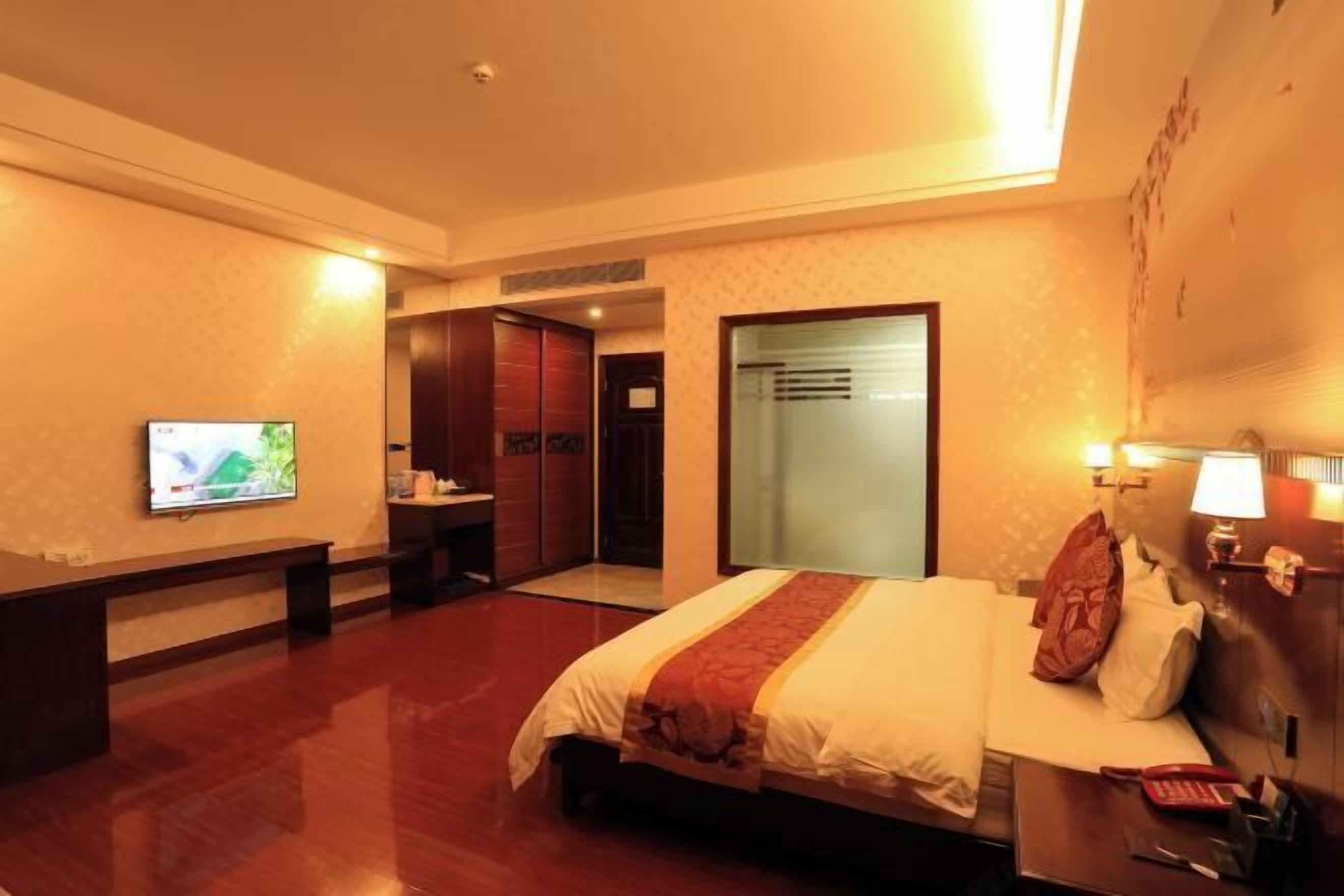 A hotel room with a bed, a desk, a television, and a door leading to a bathroom.