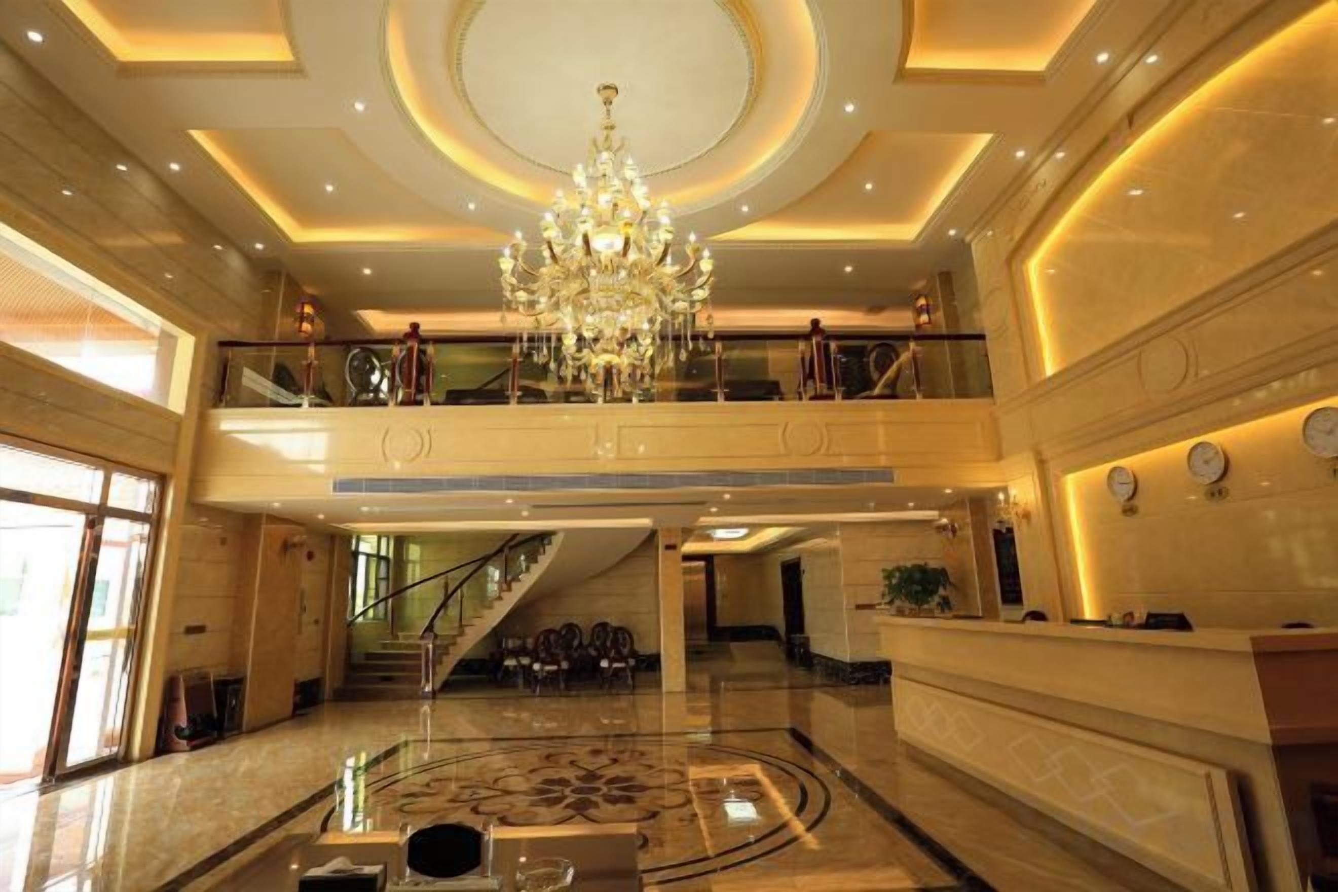 Um hall amplo com um lustre imponente, uma escadaria e um balcão de recepção.