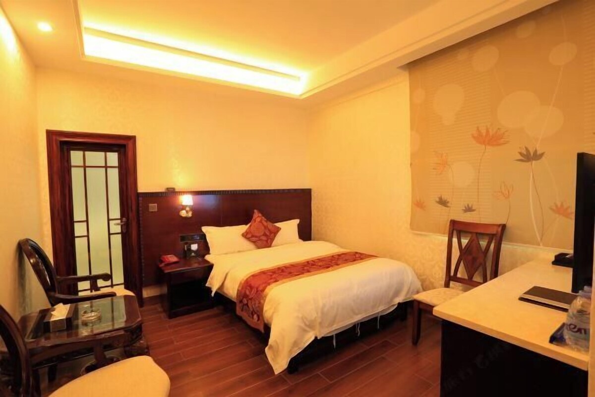 A hotel room with a bed, bedside table, lamp, chair, desk, and a television.