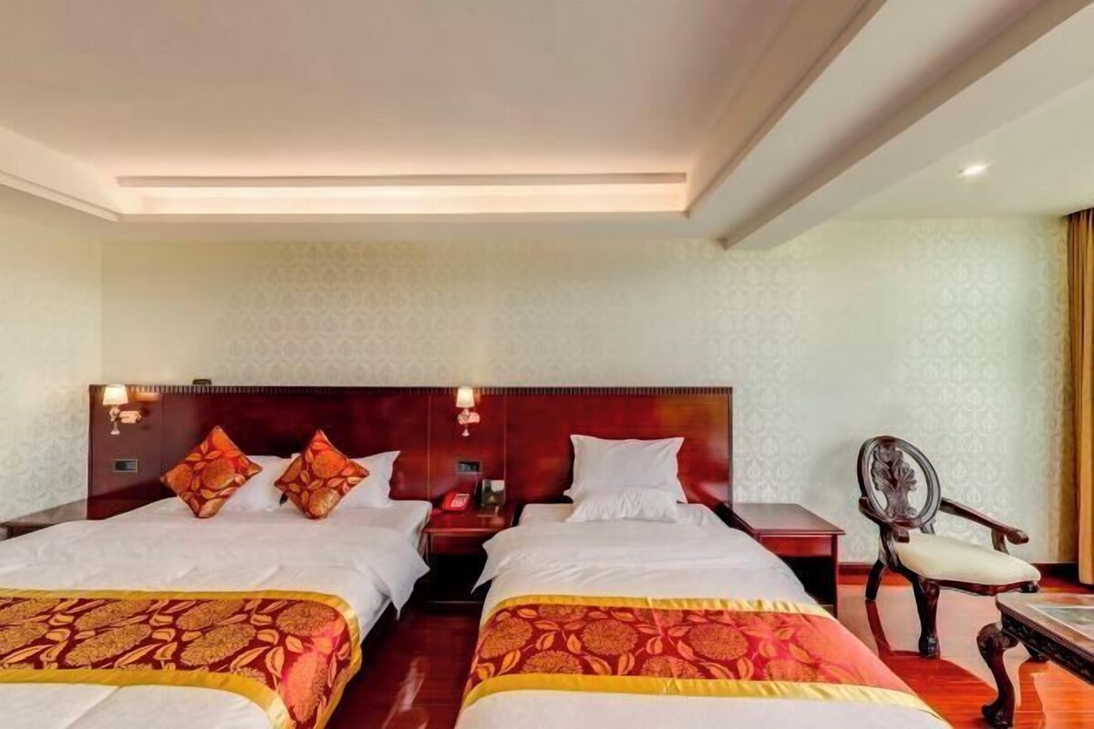 A hotel room with two beds, a nightstand, a chair, and a patterned wall.