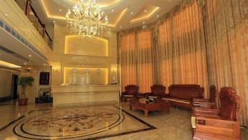 A spacious lobby with a grand chandelier, a reception desk, and a large, ornate carpet.