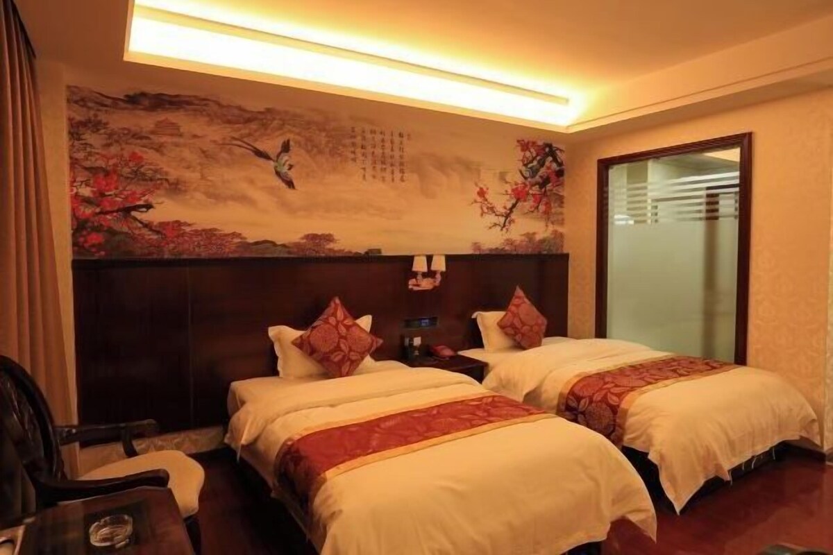 A hotel room with two beds, a nightstand, a chair, and a wall with a painting.