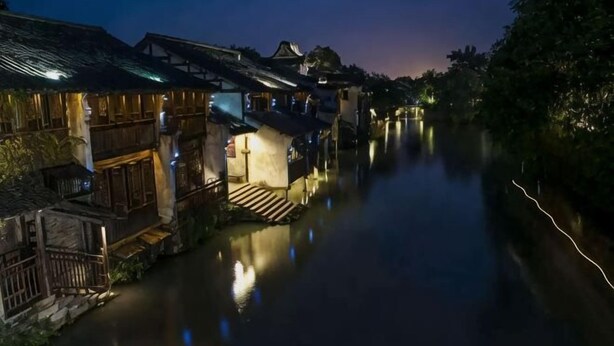 A narrow waterway flanked by traditional buildings with illuminated windows and doors. - Xingfu Yayuan Guesthouse (Tongxiang)