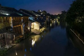 Een smalle waterweg langs traditionele gebouwen met verlichte ramen en deuren.