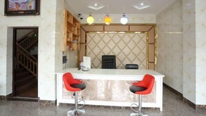 A reception area with a white counter, two red bar stools, a black office chair, and a television mounted on the wall. - Xingfu Yayuan Guesthouse (Tongxiang)
