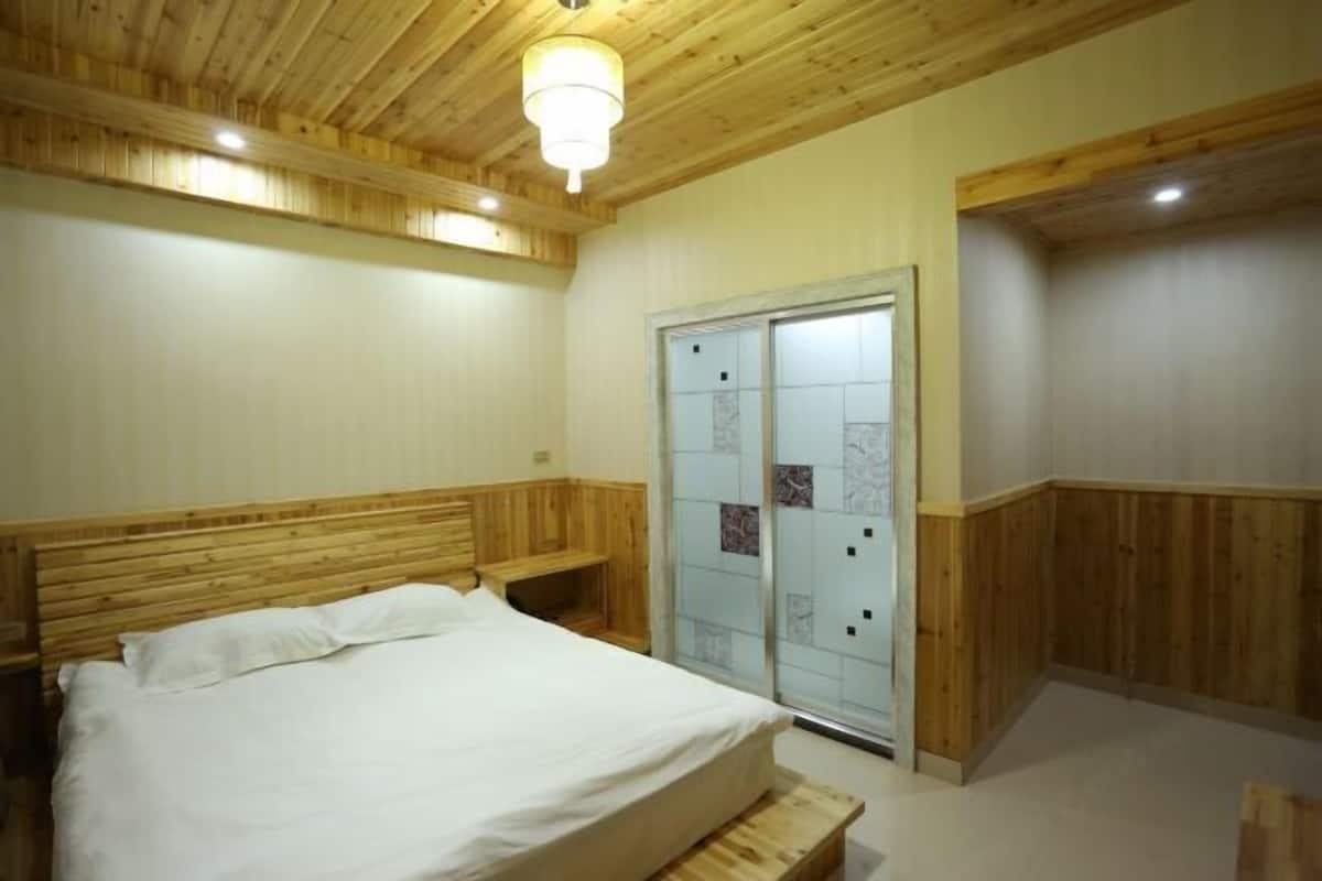 Un dormitorio con cabecera de madera, cama con ropa de cama blanca, banco de madera y puerta corredera de vidrio con panel satinado.