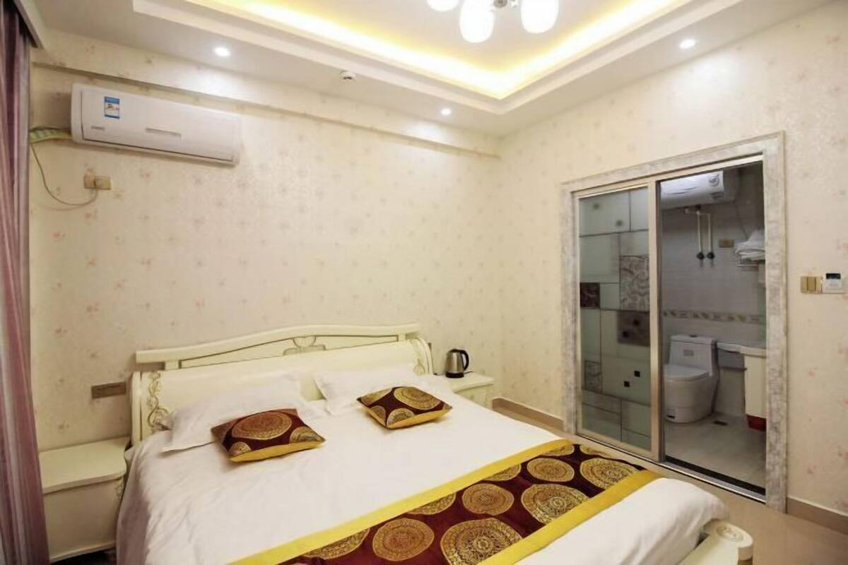 Una habitación de hotel con cama, mesita de noche y baño con mampara de vidrio.