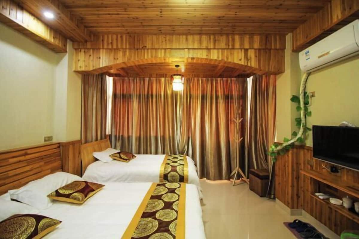Habitación de hotel con paneles de madera, dos camas con cubrecamas estampados, un televisor y una planta.