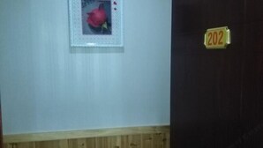 A room with a wooden wall paneling, a framed picture of a pomegranate, and a door with a number plate indicating room 202. - Xingfu Yayuan Guesthouse (Tongxiang)